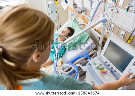 High angle view of nurse pressing monitor\'s button with patient lying on bed in hospital