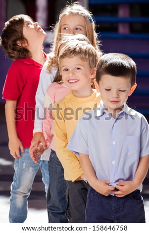 Portrait of cute boy standing with friends in a row at kindergarten