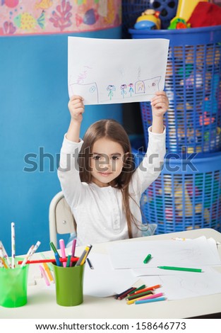 Portrait of cute preschool girl showing drawing paper in art class