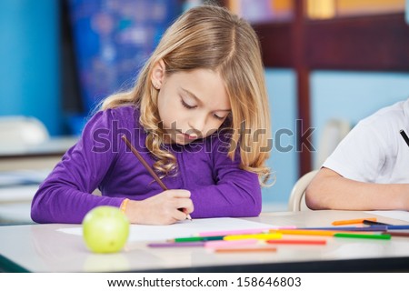 Pretty little girl with sketch pen drawing in kindergarten