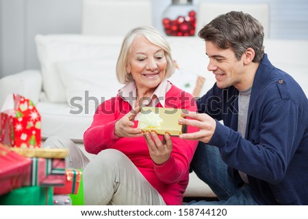 Happy son giving Christmas gift to mother at home