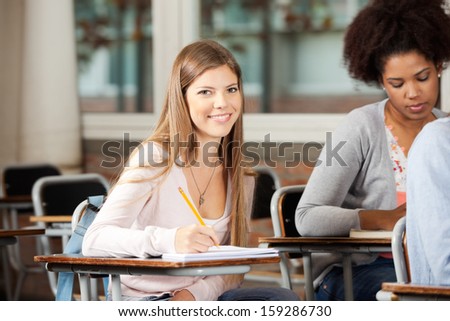 Portrait of happy female student sitting at desk with classmates in classroom