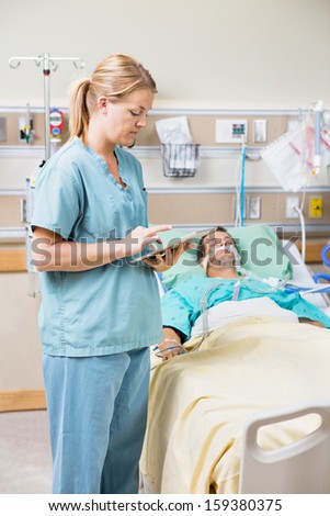 Nurse using digital tablet while patient resting on bed in hospital