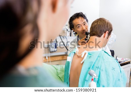 Portrait of mid adult doctor with otoscope examining patient\'s ear in hospital