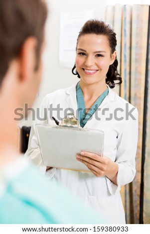 Portrait of beautiful doctor with clipboard standing by patient in hospital