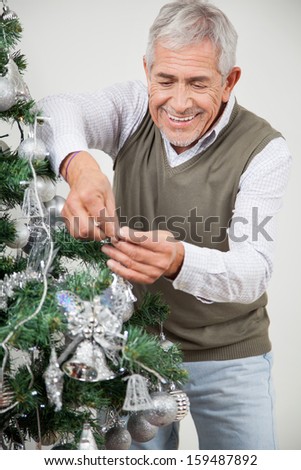 Happy senior man decorating Christmas tree with silver ornaments at home