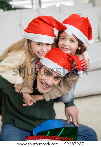 Portrait of happy father piggybacking children during Christmas at home