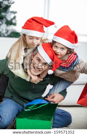Portrait of happy father piggybacking children during Christmas at home