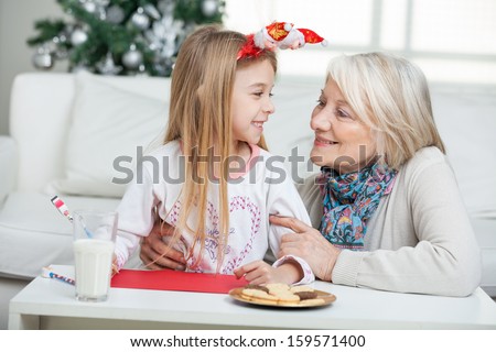Happy grandmother and girl with cardpaper looking at each other during Christmas at home