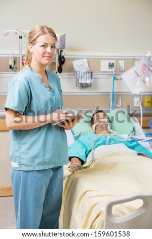 Portrait of nurse with digital tablet while male patient resting on bed in hospital room