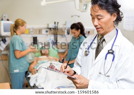 Male doctor writing notes while nurses examine patient in emergency
