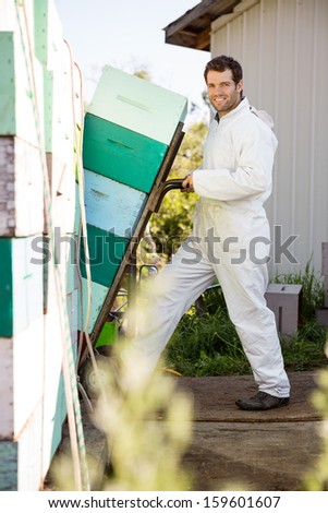 Full length portrait of young beekeeper loading stacked honeycomb crates in truck