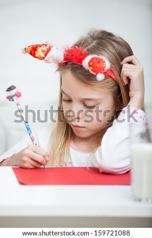 Cute girl wearing headband writing letter to Santa Claus at home