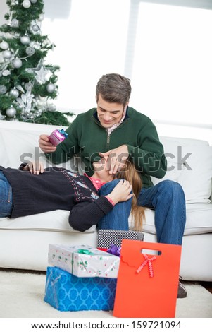 Man covering woman's eyes while holding gift during Christmas at home