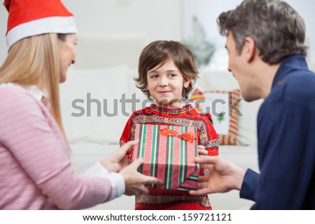 Smiling boy receiving Christmas gift from parents at home