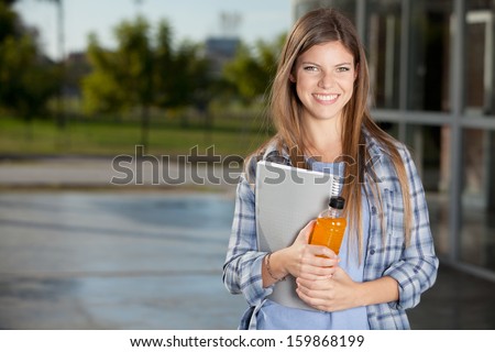 Candid portrait of a University Student standing with notes and drink
