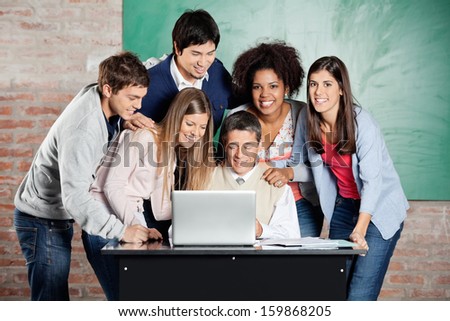 Portrait of female students standing with classmates while teacher teaching on laptop in classroom