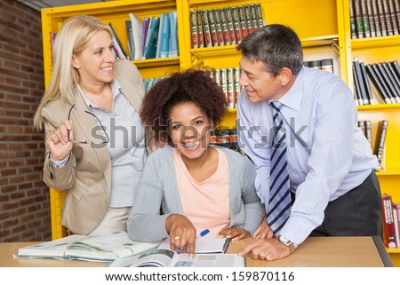 Portrait of cheerful female student with teachers looking at each other in university library
