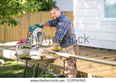 Portrait of happy mid adult carpenter cutting wood using table saw at construction site