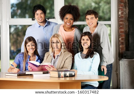 Portrait of happy students and teacher with books smiling at desk in classroom