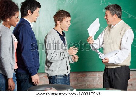 Happy male professor showing test result to successful male student in classroom