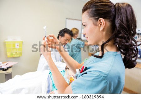 Nurse preparing injection while doctor and colleague treating patient in hospital