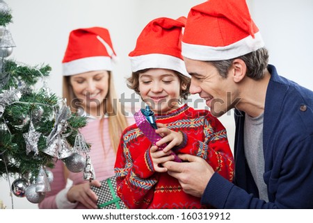 Happy father and son opening Christmas gift with mother in background at home