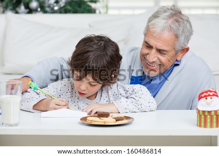 Grandfather assisting boy in writing letter to Santa Claus during Christmas at home