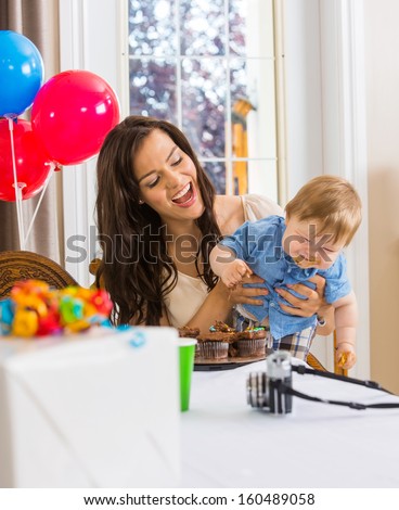 Mid adult mother holding baby boy with messy hands covered with cake icing at birthday party