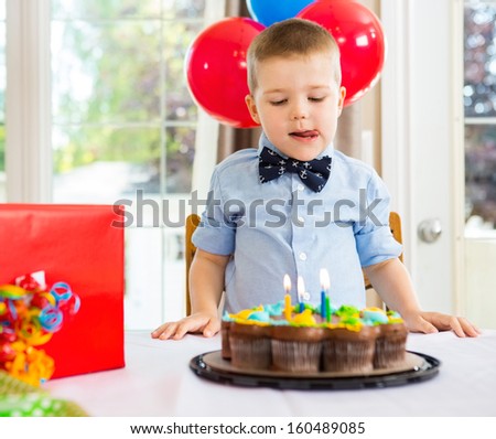 Birthday boy licking lips while looking at cake on table