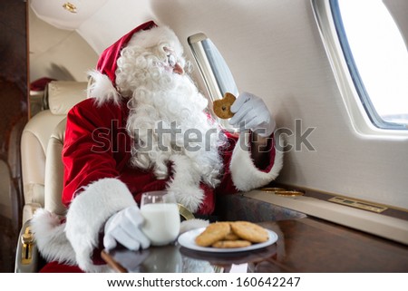 Man in Santa costume holding cookie while looking through private jet\'s window