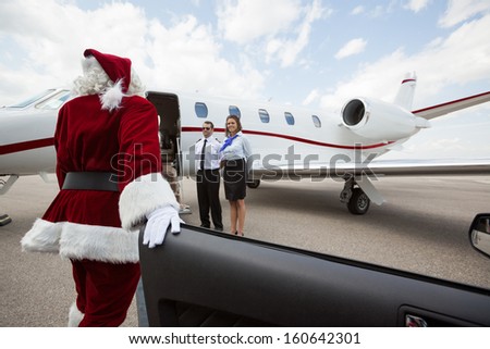 Santa disembarking car while walking towards private jet with pilot and airhostess standing by