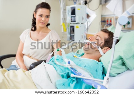 Woman looking at young patient resting on bed in hospital