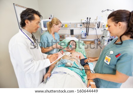 Doctor holding clipboard while nurses treating critical male patient in hospital