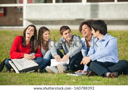 Cheerful multiethnic college students sitting on grass at campus
