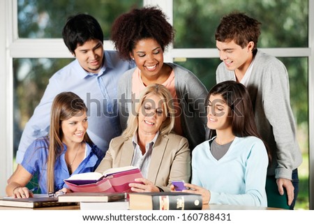 Mature female professor and students discussing over book in classroom