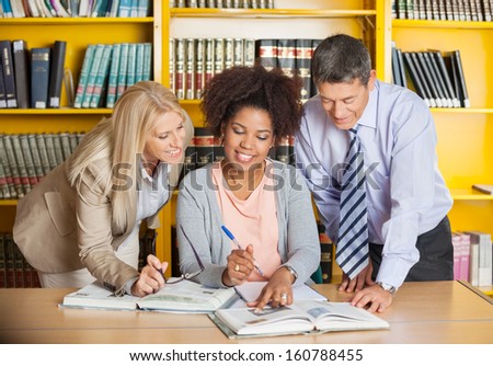 Mature college teachers assisting student with studies in library