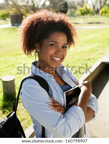 Portrait of happy young woman standing arms crossed on college campus