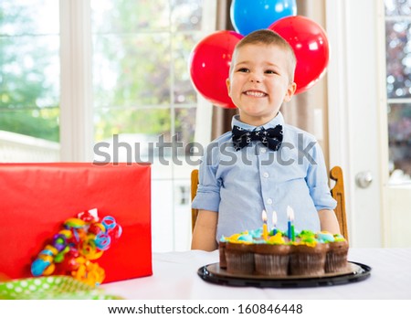 Excited birthday boy with cake and present on table at home