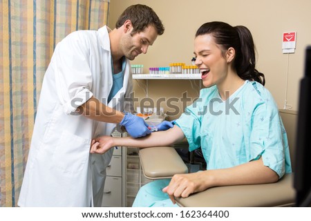 Young patient screaming while doctor drawing blood sample in hospital room