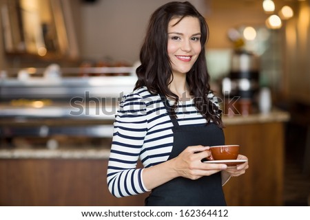 Portrait of beautiful waitress holding coffee cup while standing in cafeteria