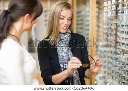 Young woman examining eyeglasses with salesgirl in optician store