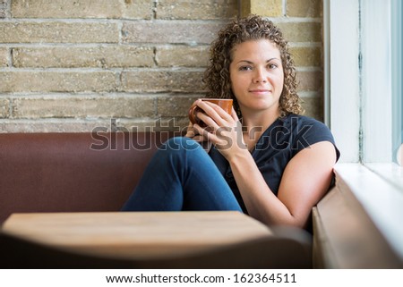 Portrait of beautiful mid adult woman with coffee mug sitting in cafeteria