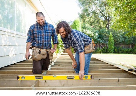 Construction worker checking level of wood with spirit level while coworker looking at it