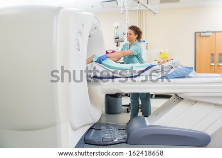 Mid Adult Nurse Preparing Patient For Ct Scan Test In Examination Room