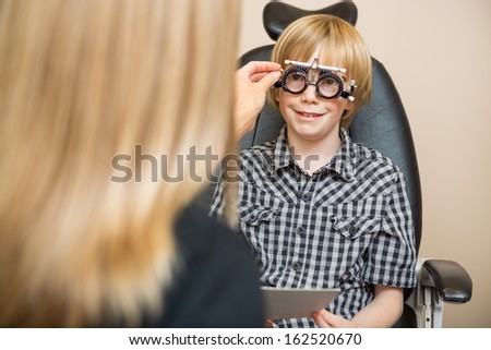 Female optician determining prescription values with optometric frame for boy in store