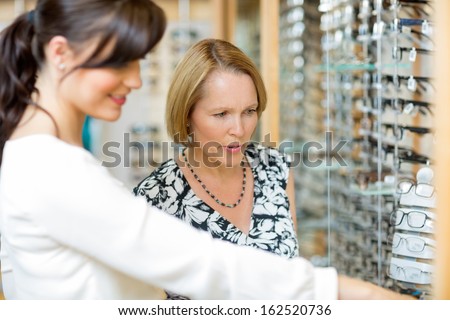 Salesgirl assisting senior woman in selecting glasses at optician store