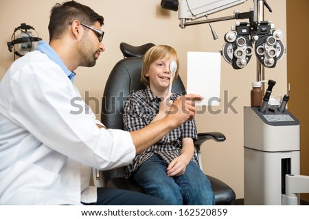 Boy looking at vision test with one eye covered with occluder