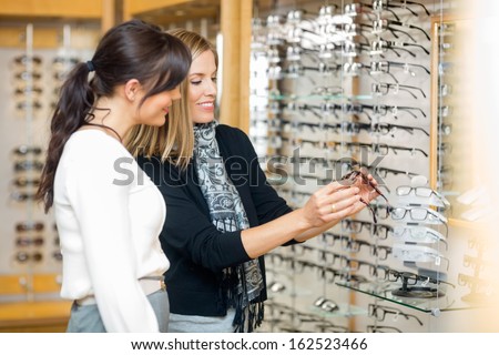 Happy Woman With Salesgirl Examining Eyeglasses In Optician Store