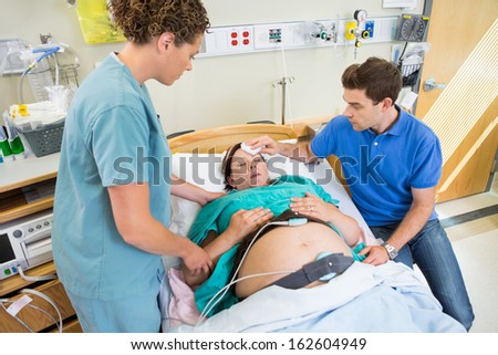 Loving mid adult man wiping forhead of pregnant woman's forehead in hospital Loving mid adult man wiping forhead of pregnant woman's forehead in hospital